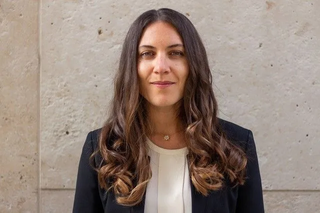 Person mit einem Blazer steht vor grauer Wand.