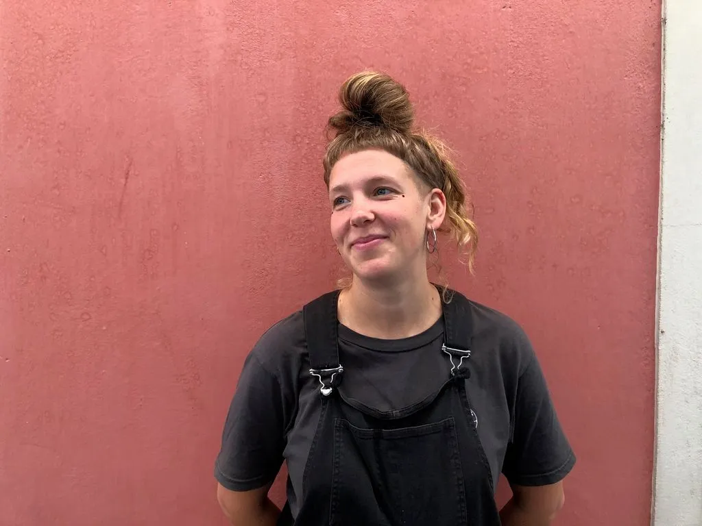 Junge Person steht lächelnd vor roter Wand.