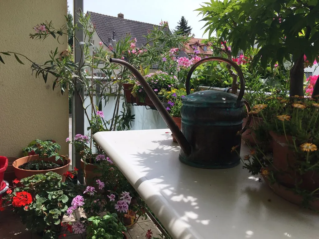 Eine kleine kunstvolle Giesskanne auf einem Balkon mit Blumen.