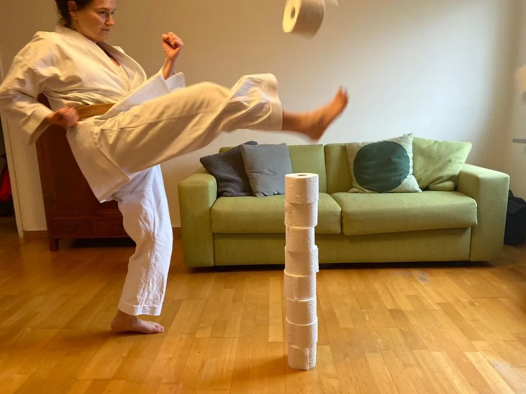 Frau macht Karatekick mit aufgestapelten WC-Rollen.