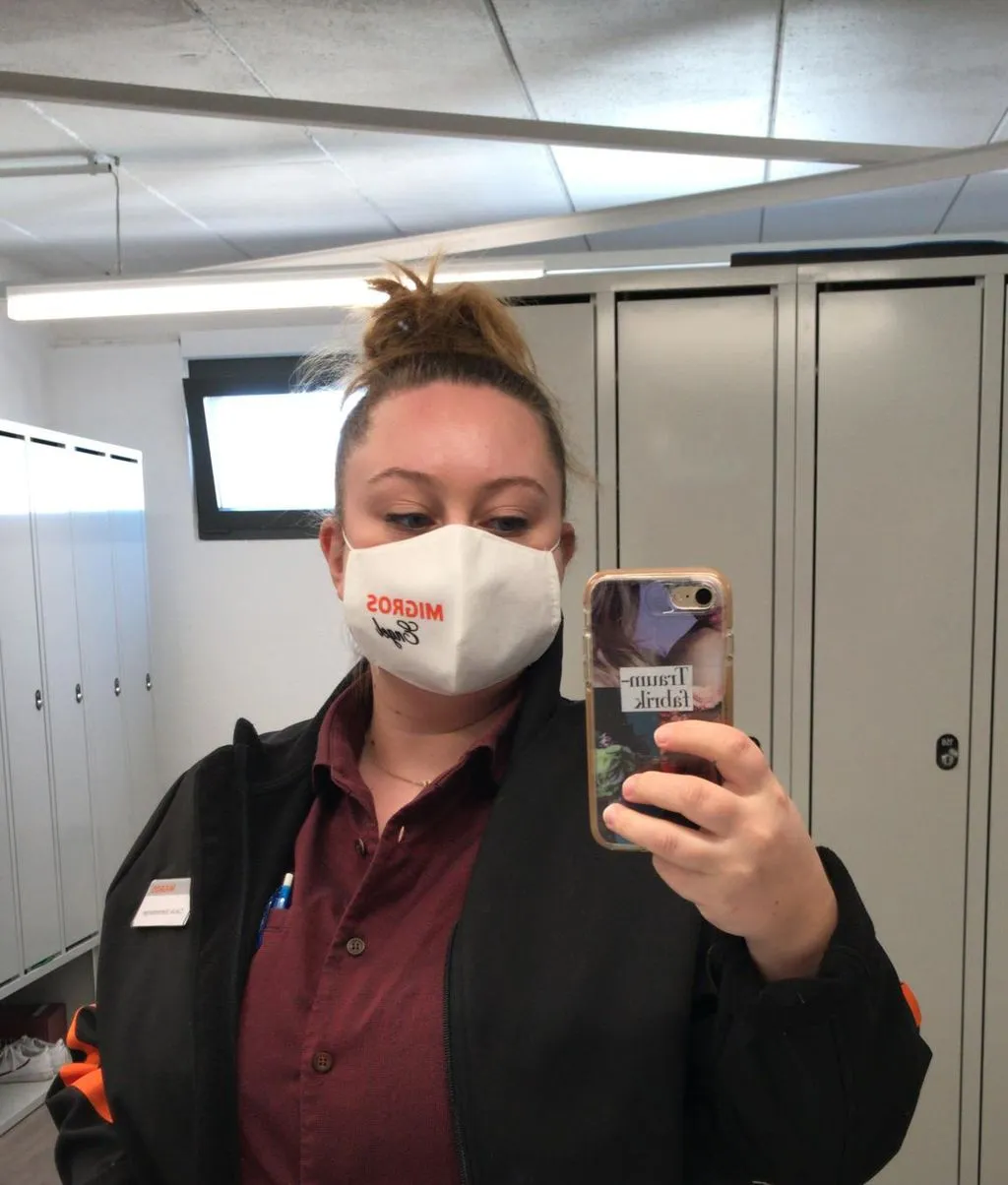 Junge Verkäuferin mit Maske macht ein Selfie vor Spiegel.