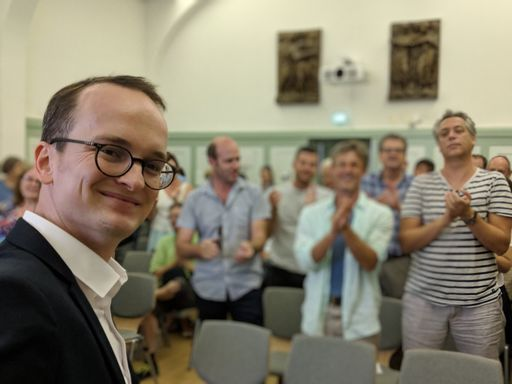 Mann mit Anzug steht vor seinem klatschenden Team.