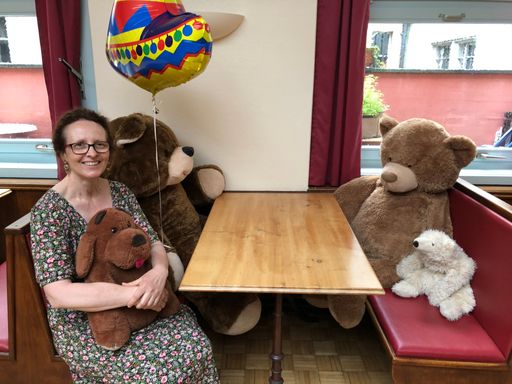 Eine Frau sitzt mit Plüschtieren an einem Restauranttisch.