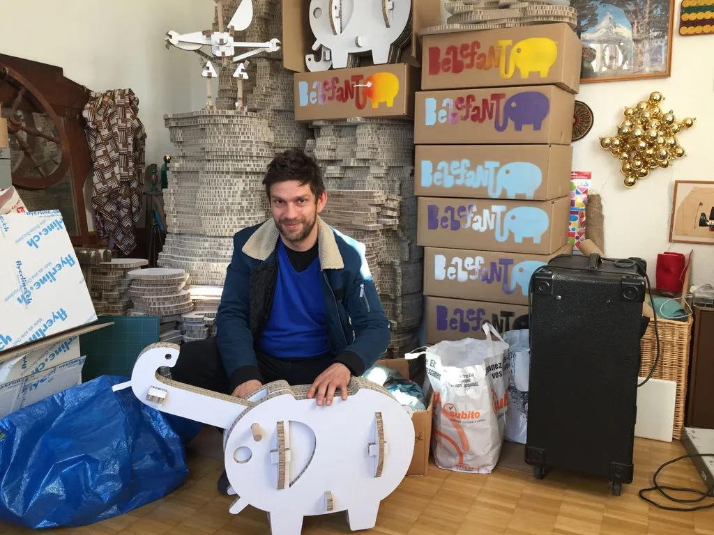 Mann hinter einem Spielzeugelephanten aus Karton.