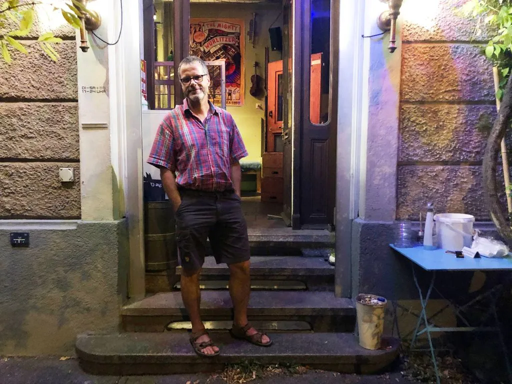 Mann in Sandalen steht vor Bar.