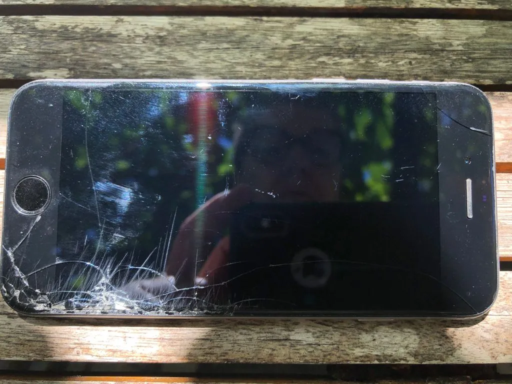 Reflektion einer Frau in einem Smartphone mit zerbrochenem Display.