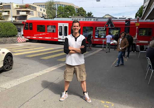 Lachender Mann mit verschränkten Armen vor Stadtbahn.