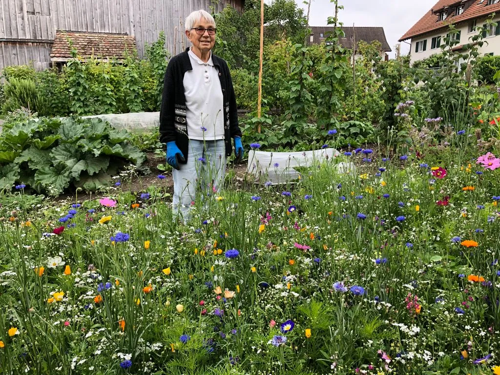 Seniorin steht inmitten Blumenwiese.