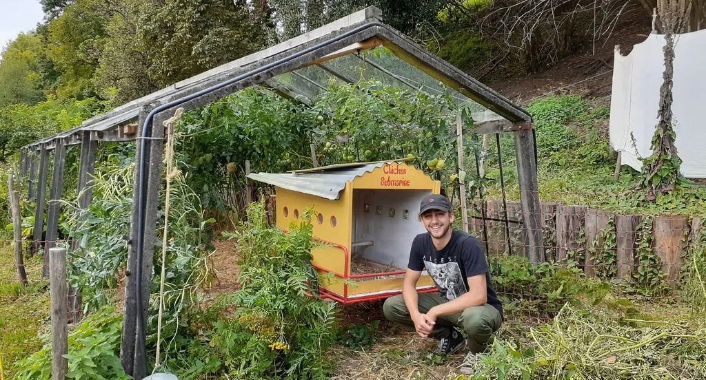 Junger Mann in einem Garten neben einem kleinen gelben Wagen